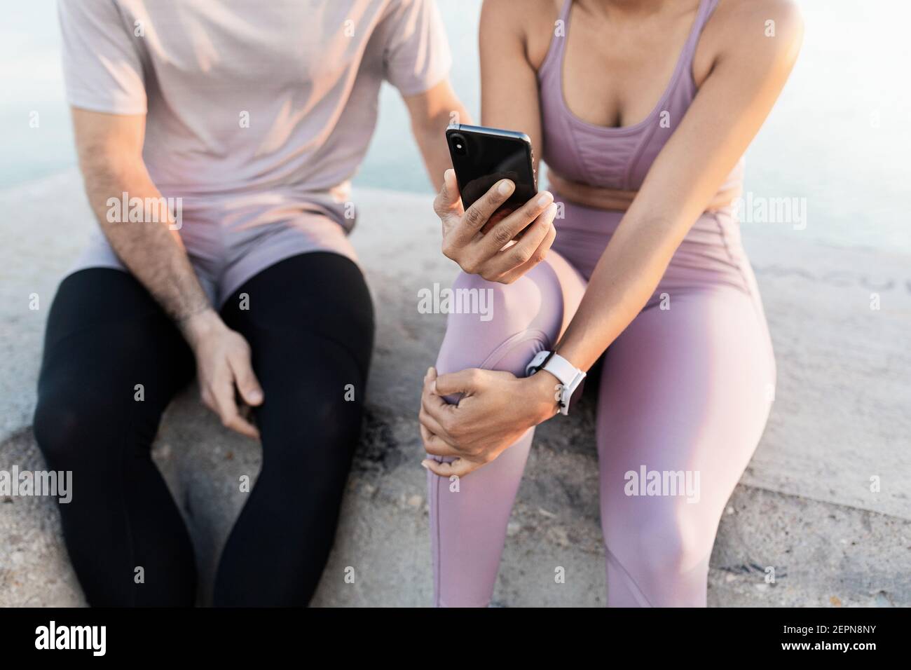Junge froh Sportler mit ethnischen weiblichen Partner in Sportkleidung Während die Zeit zusammen mit dem Handy gegen Meer nach Schulung Stockfoto