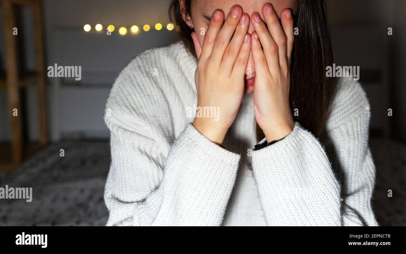 Junge Frau bedeckt das Gesicht mit den Händen, während sie allein weint Schlafzimmer zu Hause Stockfoto