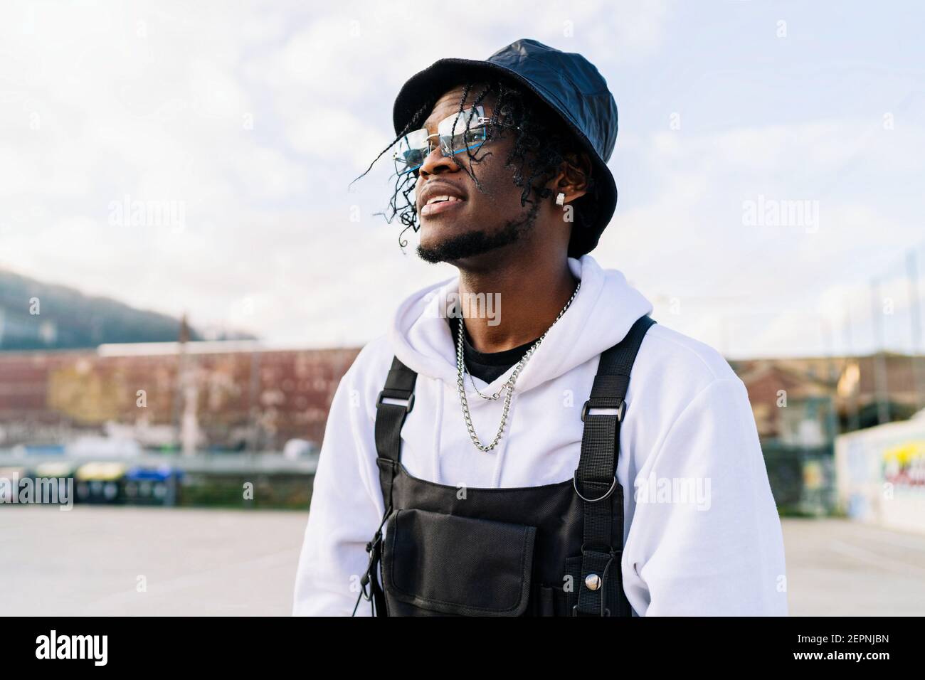 Junge trendige ethnische Mann in Sonnenbrillen tanzen beim Blick weg Gegen Graffiti Wand in der Stadt Stockfoto