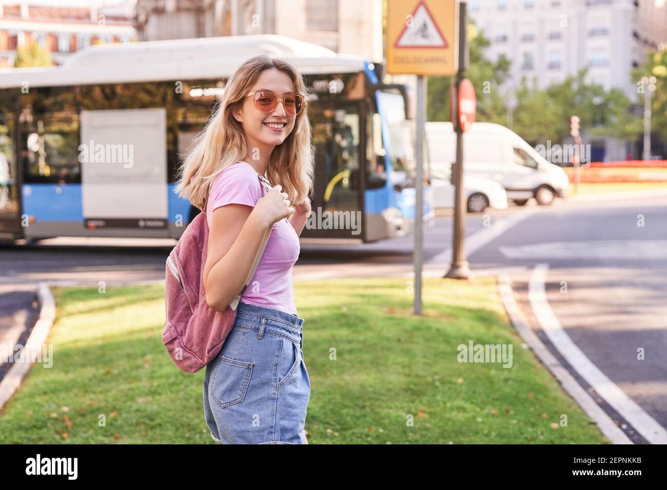 Seitenansicht der positiven teen weiblich mit Rucksack wartet auf Transport auf dem Bürgersteig während der Reise in Madrid Stockfoto