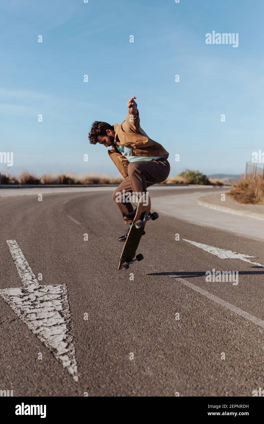 Ganzkörper junge bärtige Skater in casual Outfit springen während Durchführung Kickflip auf Skateboard auf Asphalt Straße Stockfoto