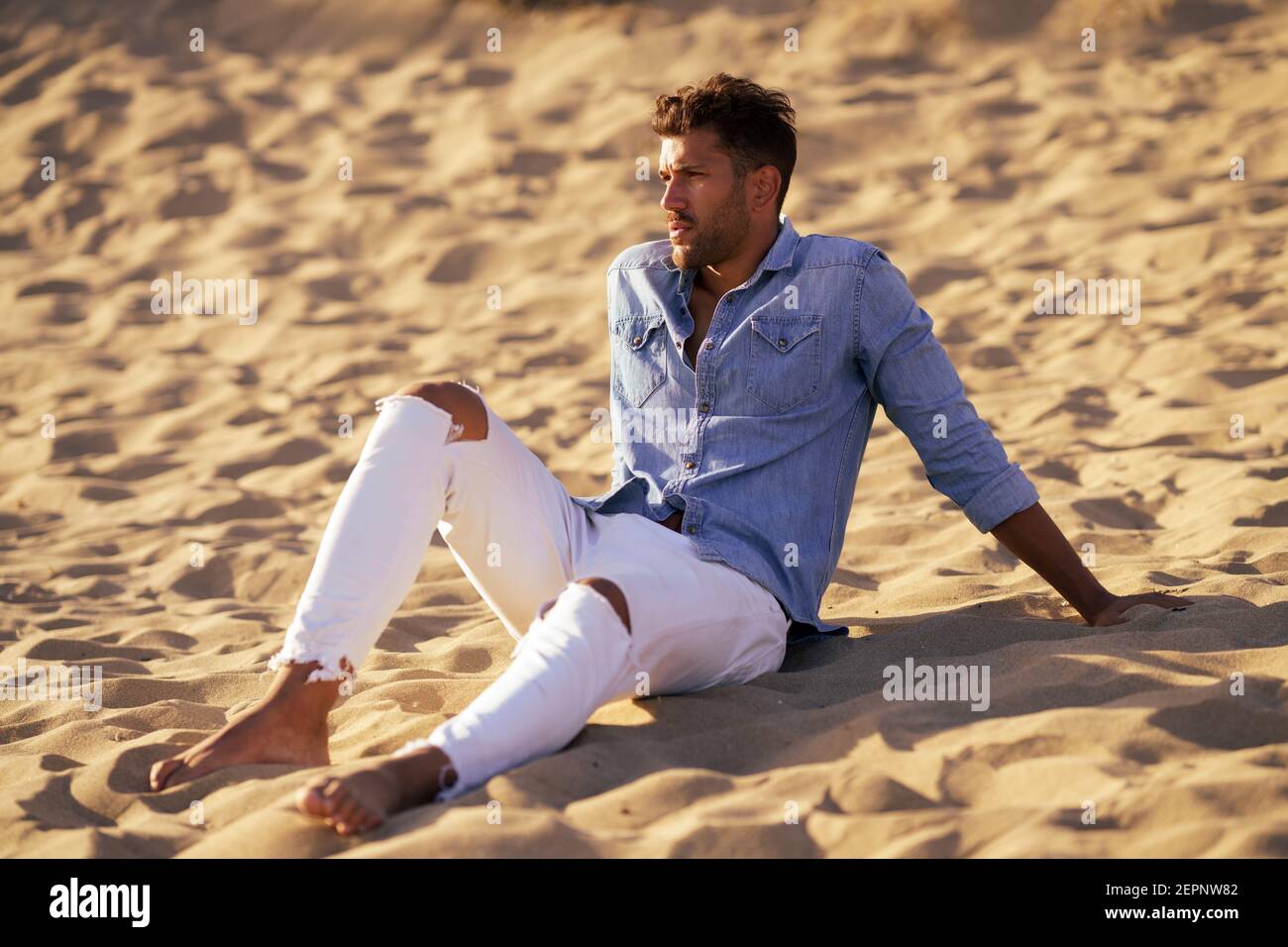 Attraktiver Mann, der auf dem Sand des Strandes sitzt Stockfoto
