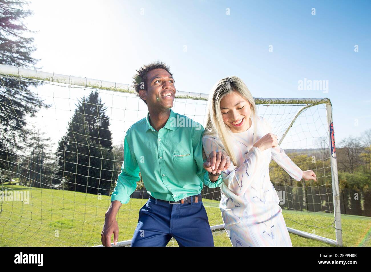 Fußball-Fashion-Geschichte mit einem schwarzen männlichen Modell und Blondine Chinesische weibliche Modell erzielte ein Tor auf einem Fußballplatz Stockfoto