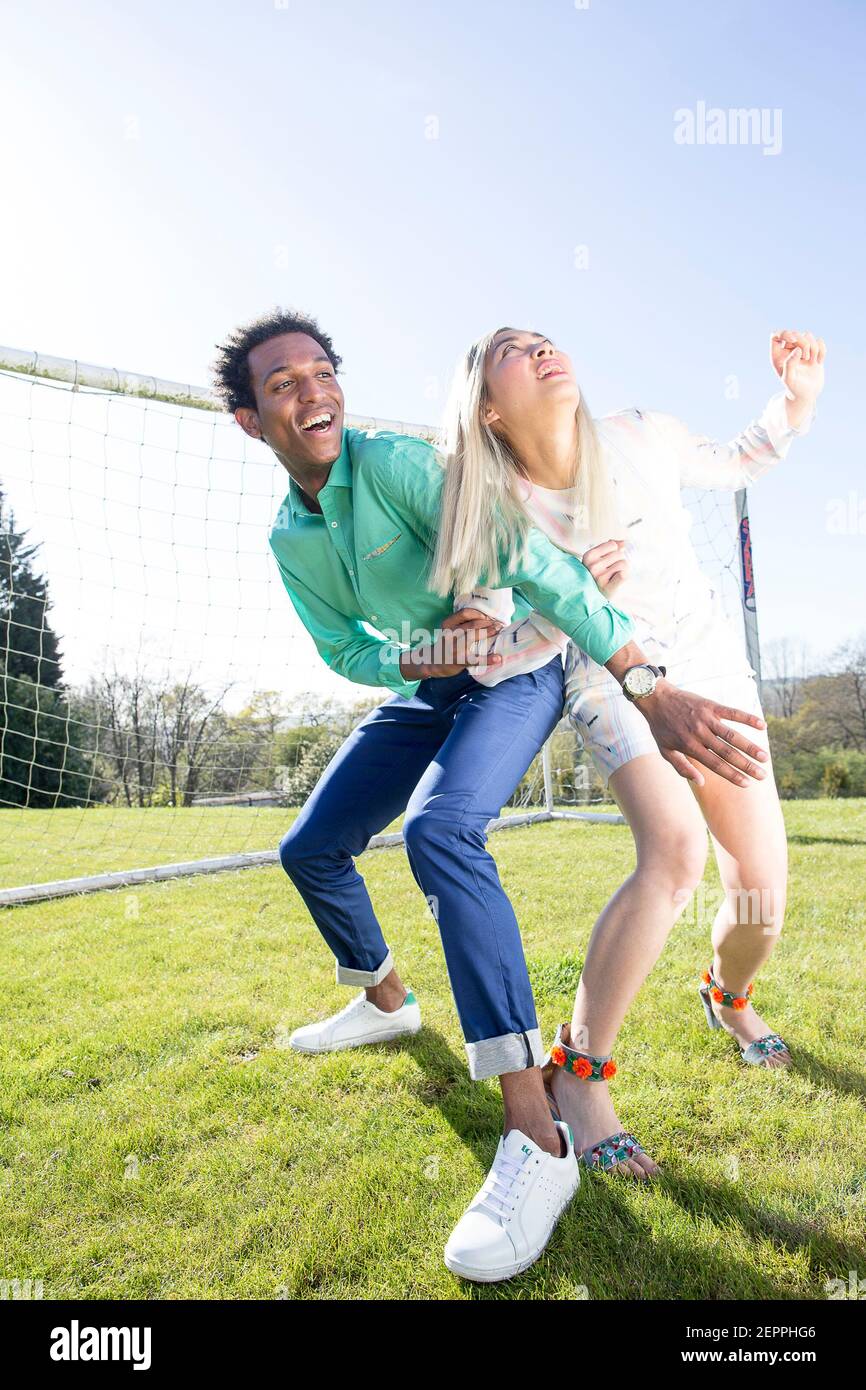 Fußball-Fashion-Geschichte mit einem schwarzen männlichen Modell und Blondine Chinesische weibliche Modell erzielte ein Tor auf einem Fußballplatz Stockfoto