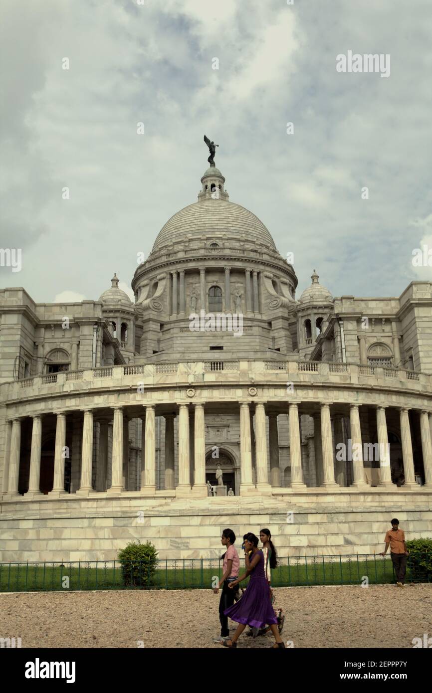 Die Besucher werden im Hintergrund der Victoria Memorial Hall in Kalkutta, Westbengalen, Indien fotografiert. Auf der Spitze der zentralen Kuppel der Halle ist eine Figur des Engels des Sieges, einer Göttin der antiken griechischen Mythologie, die den Sieg verkörpert. Stockfoto