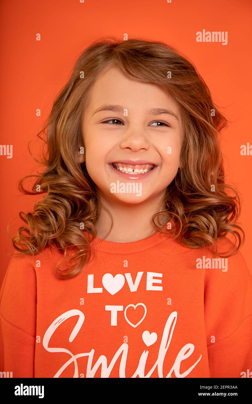 Nahaufnahme Foto von niedlichen schönen Mädchen 6-7 Jahre alt, führte lachend vor orangenen Hintergrund. Wegschauen. Toothy Smile Stockfoto