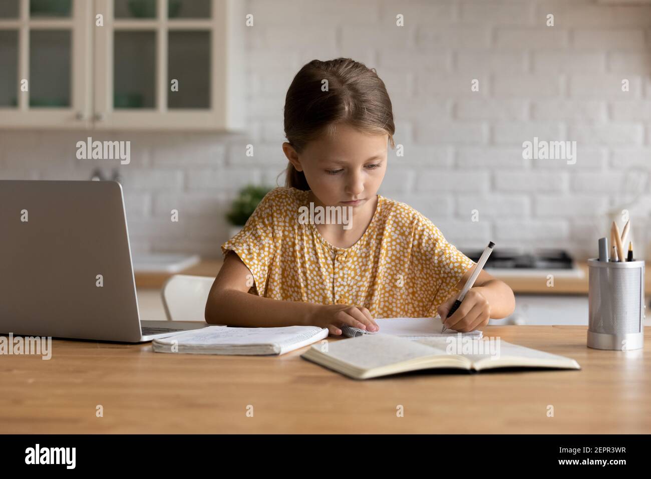 Fokussiertes kleines Schulmädchen sitzen am Schreibtisch und machen sich Notizen zum Copybook Stockfoto
