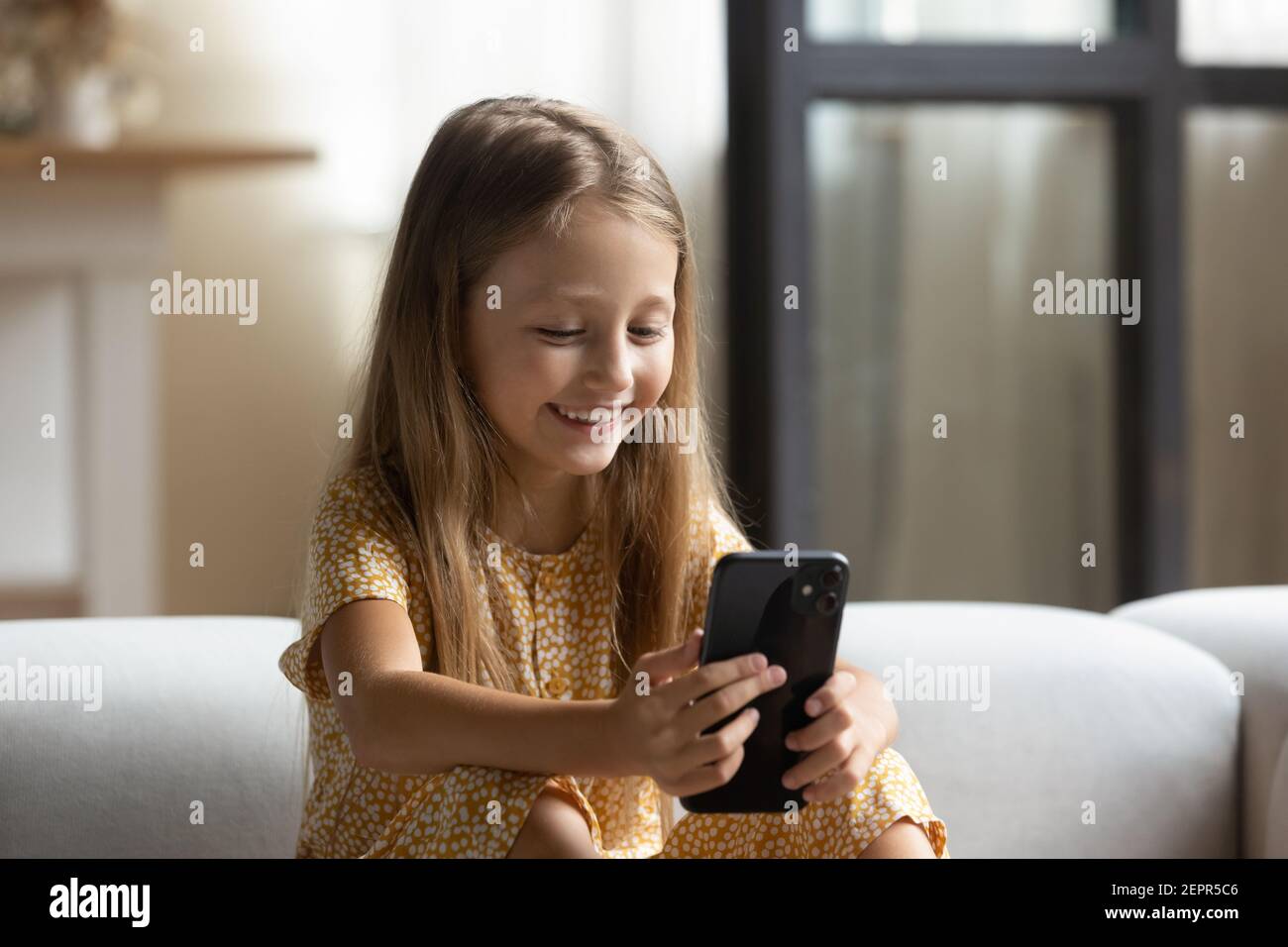 Happy kleines Mädchen sitzen auf Sofa spielen Spiel mit Handy Stockfoto