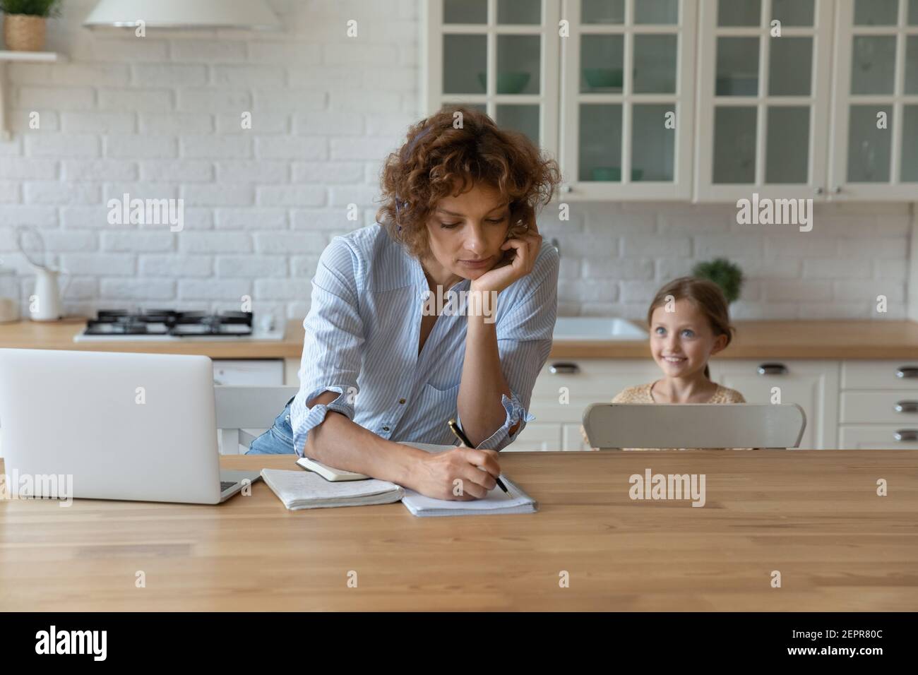 Beschäftigte Mutter beschäftigt in der Arbeit, während kleine Tochter spielen in der Nähe Stockfoto