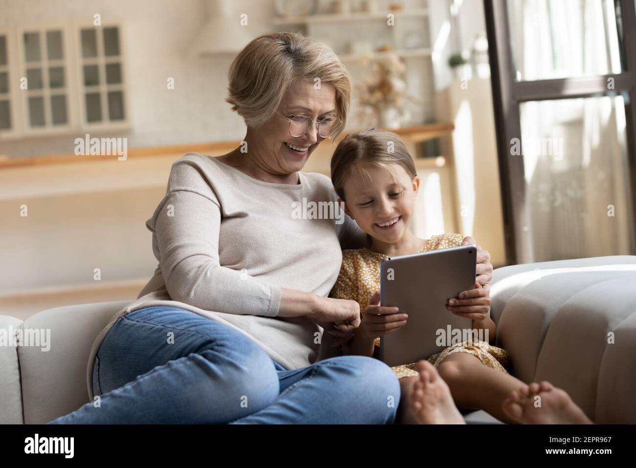 Lächelnd pensionierte Kindermädchen und kleine Mädchen beobachten Cartoon mit Tablet Stockfoto