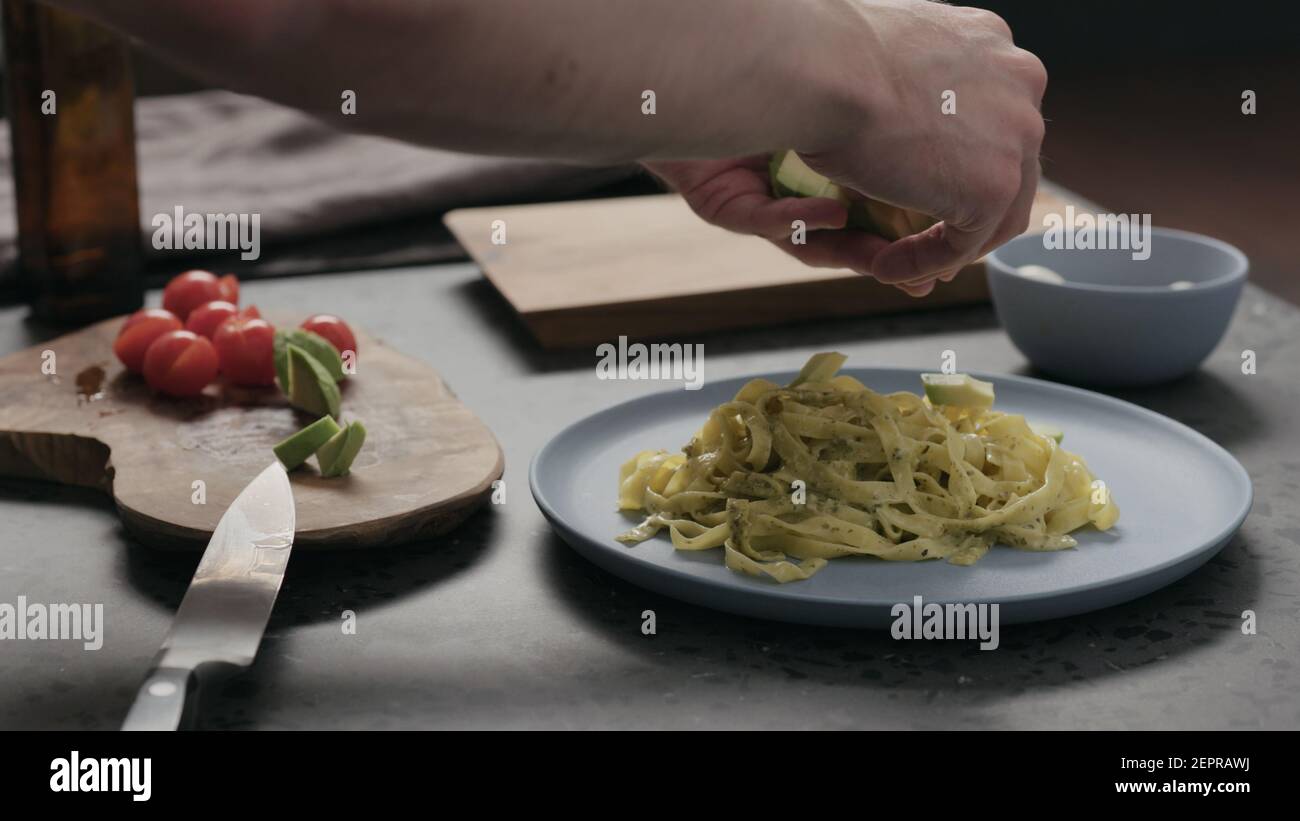 Mann fügen Avocado zu Pesto Fettuccine auf blauer Platte, breites Foto Stockfoto