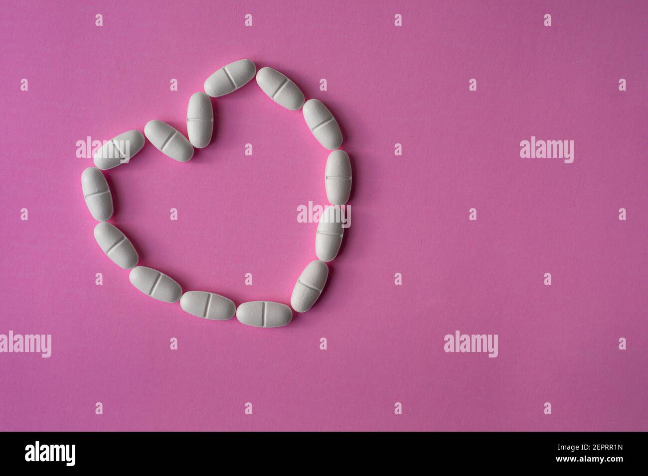 Weiße, große Pillen oder Tabletten, in einer Herzform angeordnet, um Gesundheit auf rosa Hintergrund darstellen Stockfoto
