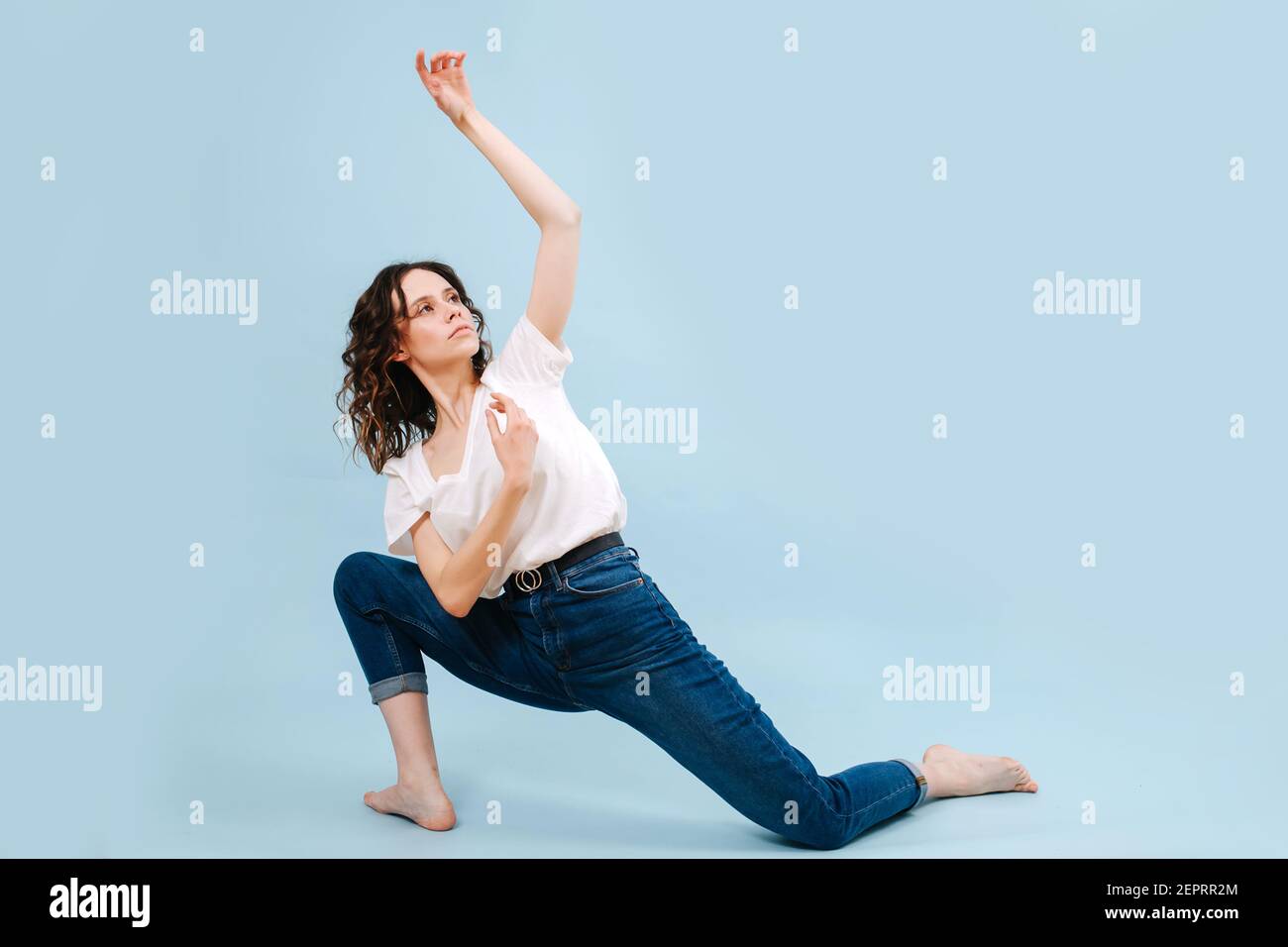 Emotionslose zeitgenössische Tänzerin posiert vor blauem Studiohintergrund. Ihre Beine in einem Ausfallschritt, Körper in entgegengesetzter Richtung verdreht. Macht Bewegungen mit h Stockfoto