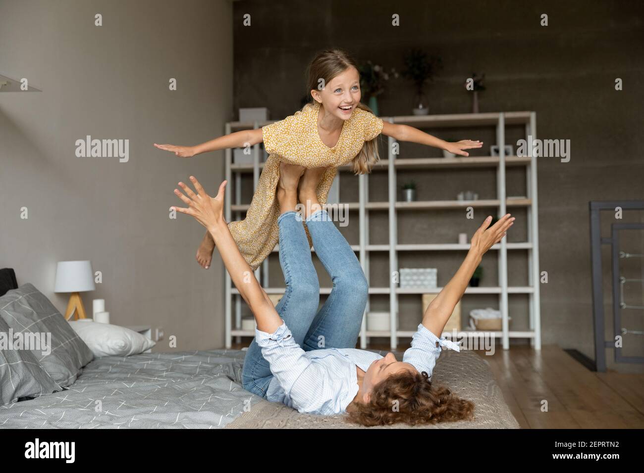 Fröhliche kleine Mädchen spielen Flugzeug fliegen mit Hilfe von Mama Stockfoto