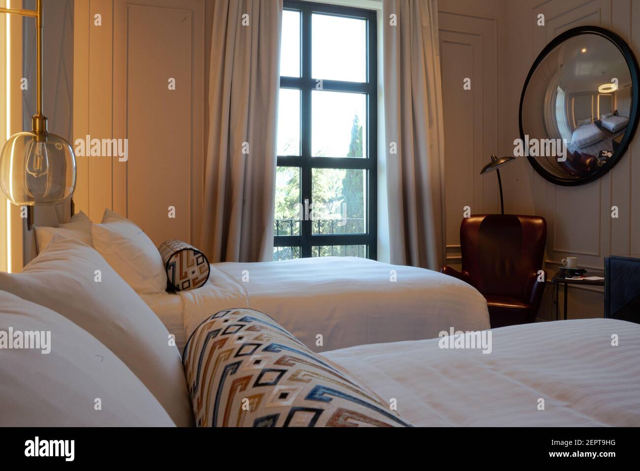 Ein gemütliches, modernes Luxus-Schlafzimmer mit zwei Einzelbetten, einem luxuriösen bequemen Stuhl mit roten Lederpolstern und einem kugelförmigen Spiegel Stockfoto