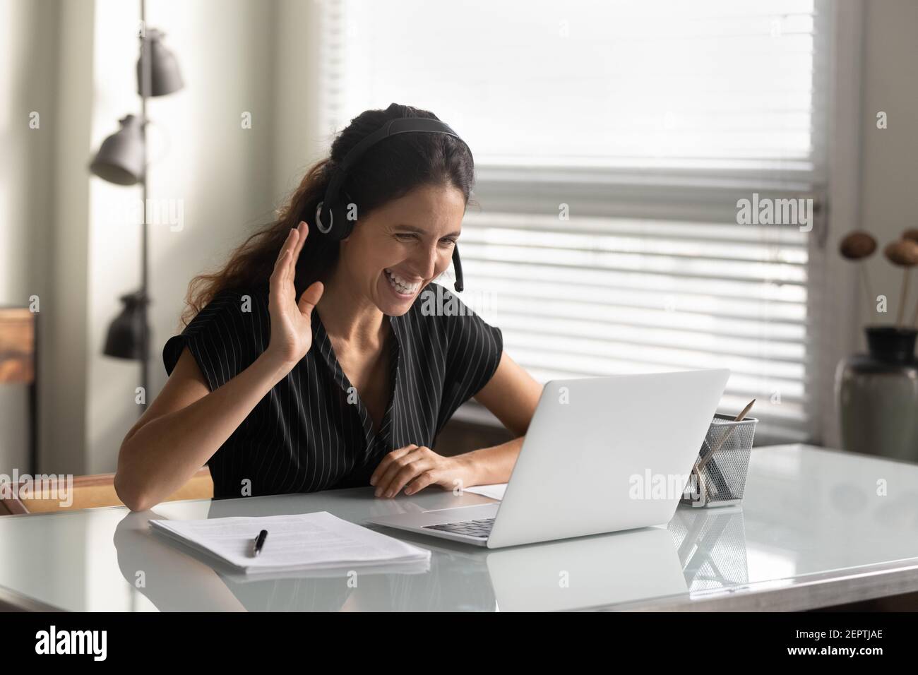Überglücklich Frau trägt Kopfhörer winkende Hand, Blick auf Laptop-Bildschirm Stockfoto