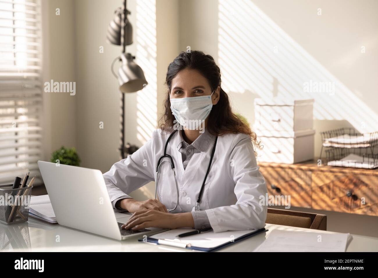 Portrait professionelle weibliche Arzt trägt Maske am Schreibtisch sitzen Stockfoto