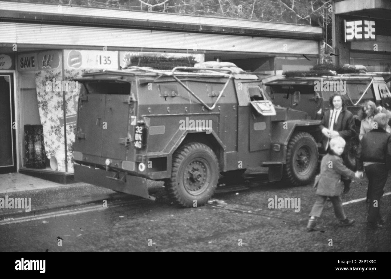 Menschen, die während der Unruhen in Nordirland 70s an einem britischen Militärpanzerwagen in einer Straße in der Innenstadt von Belfast vorbeigingen Stockfoto