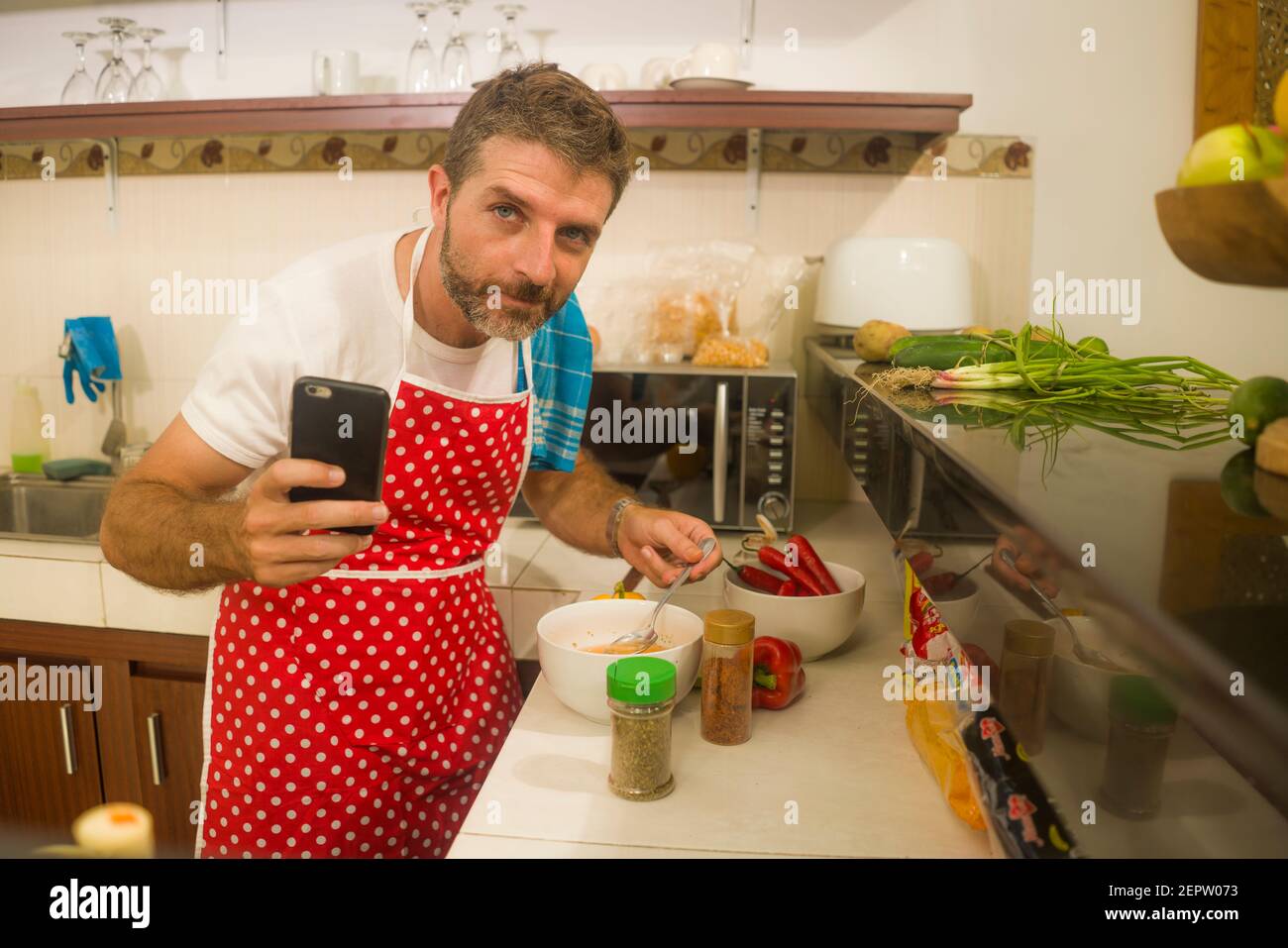 Hauskoch bei der Arbeit - jung glücklich und attraktiv zu Hause Koch Mann  in roten Schürze nach Online-Rezept im Internet Handy Kochen gesundes Essen  relaxe Stockfotografie - Alamy