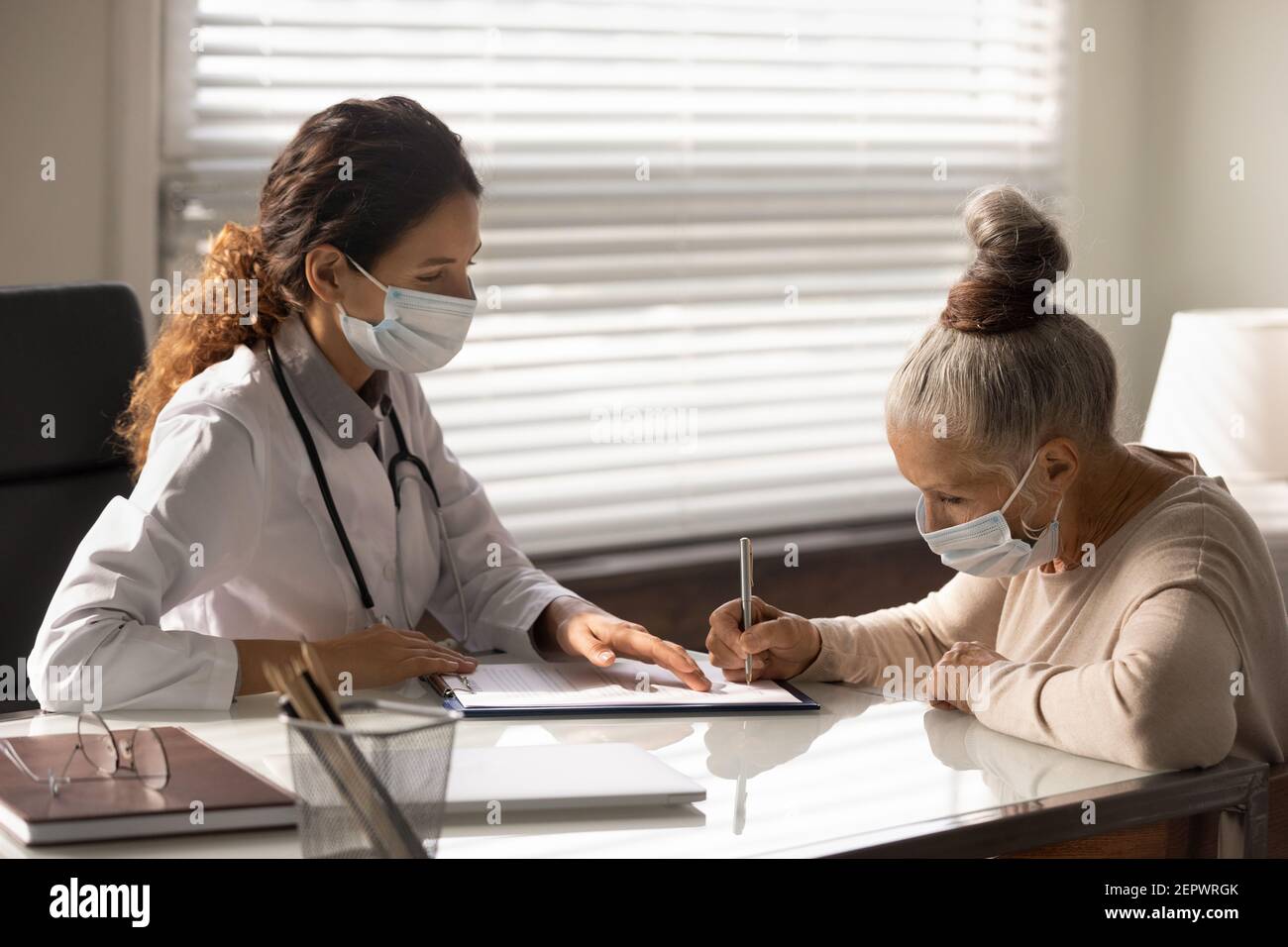 Reife Frau Patient trägt Maske Unterzeichnung Vertrag in Arztpraxis Stockfoto