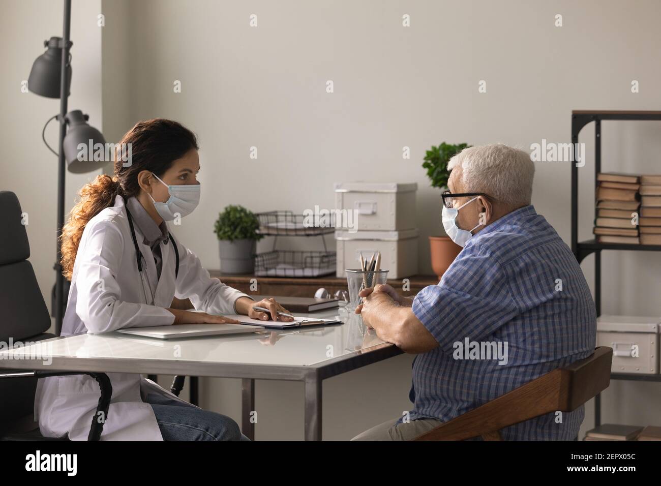 Ärztin und ältere Patientin tragen Gesichtsmasken und sprechen Stockfoto