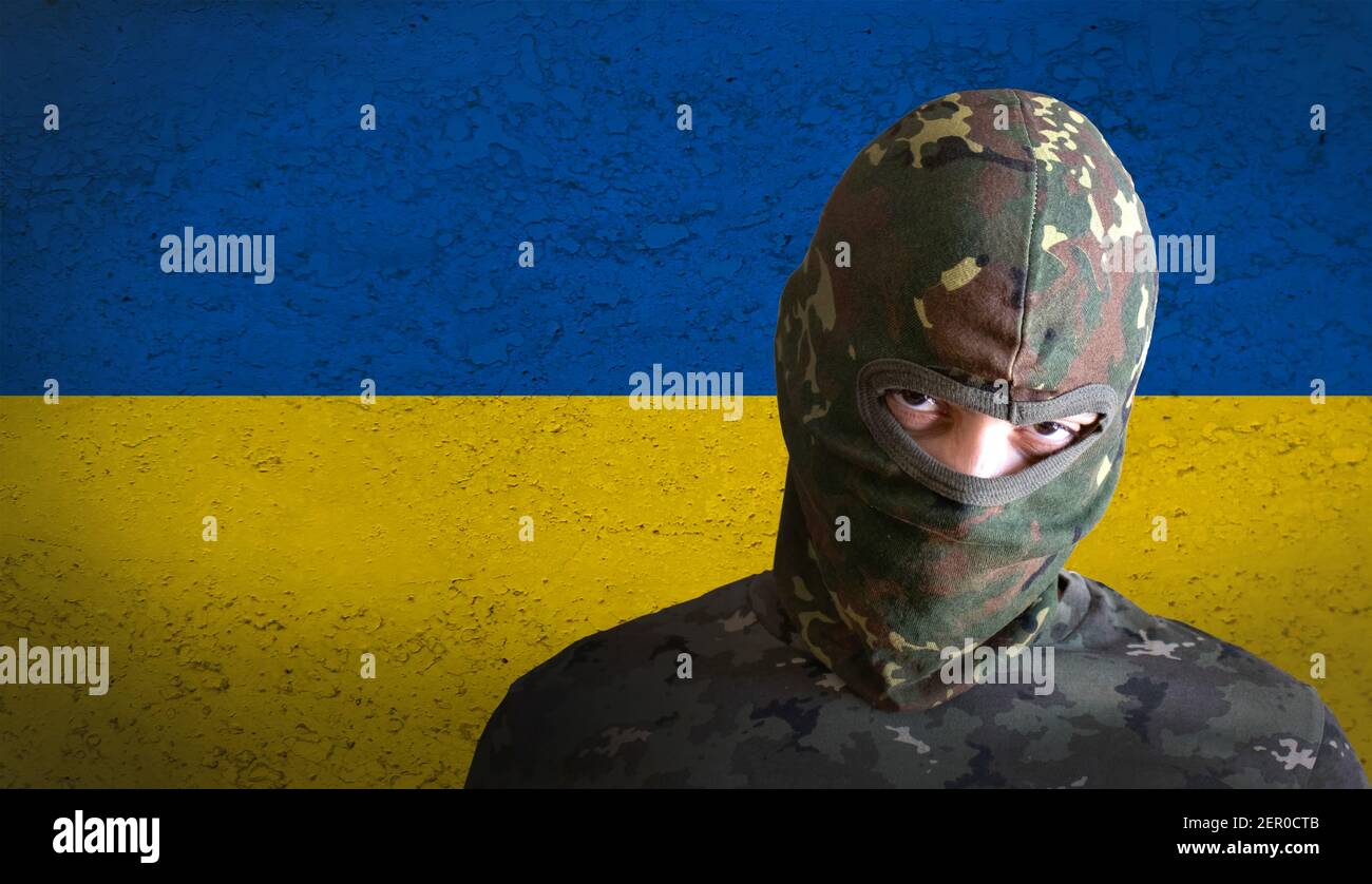 ukrainischer wütender Soldat mit ukraine-Flagge dahinter. Militärmann mit Tarnung und wütend aggressiv für den Krieg. Stockfoto