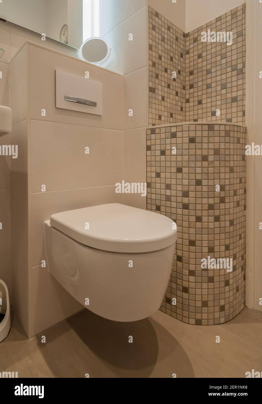 Moderne Toilettenanlage mit hellbraunen Fliesen. Zusätzlich eine dekorativ verkleidete Wand mit Mosaik Stockfoto