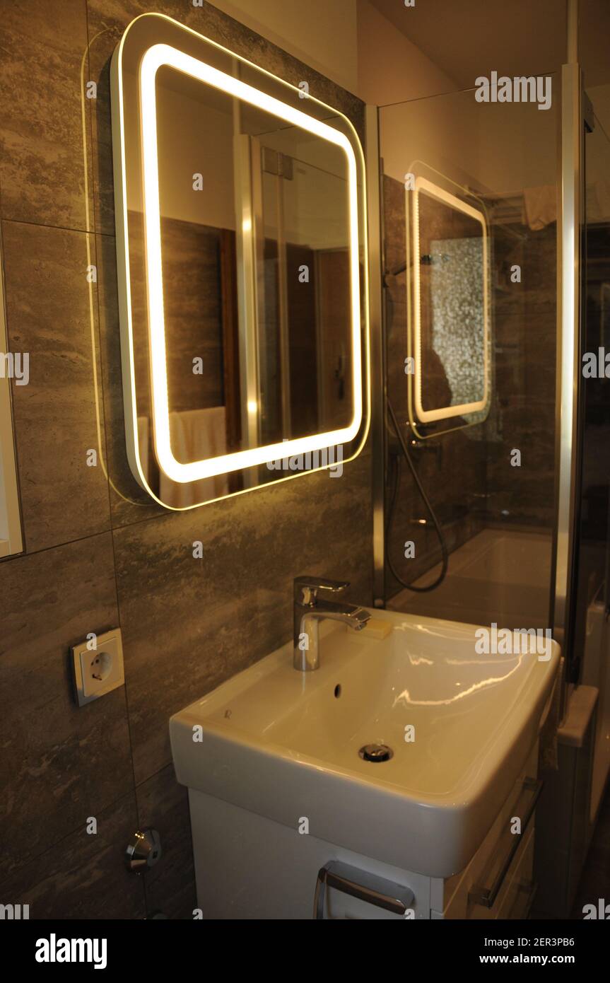 Detailansicht eines Badezimmers, mit Blick auf den Waschtisch mit beleuchtetem Spiegel. Der eingeschaltete Spiegel schafft eine gemütliche Atmosphäre Stockfoto