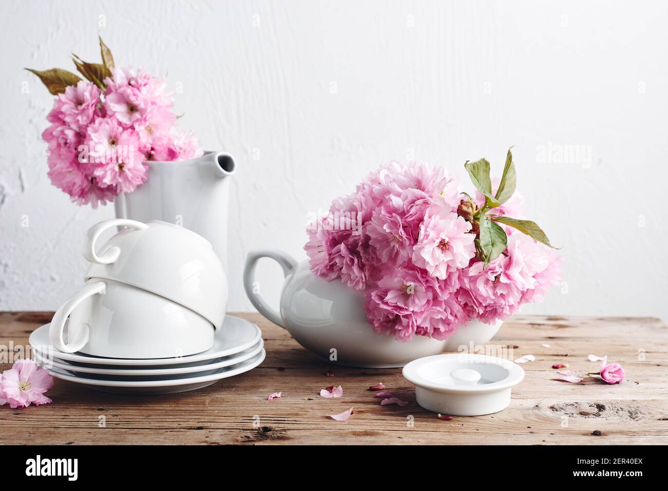 Weiße Tassen, Teekanne und rosa japanische Kirschblüten. Stillleben im Frühling. Stockfoto