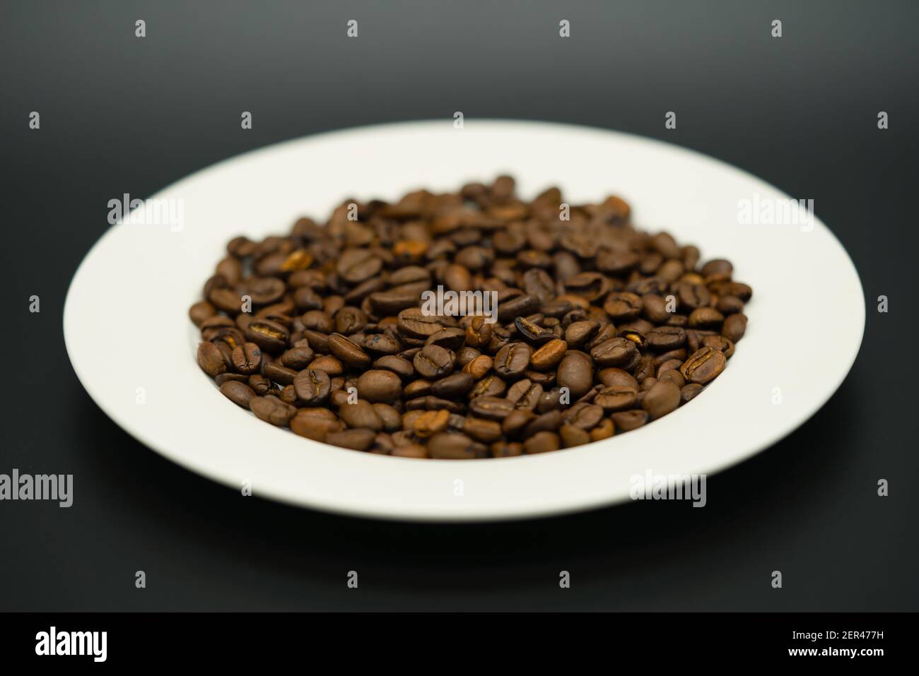 Weißer Teller voller aromatischer Kaffeebohnen gegen eine dunkle Hintergrund Stockfoto