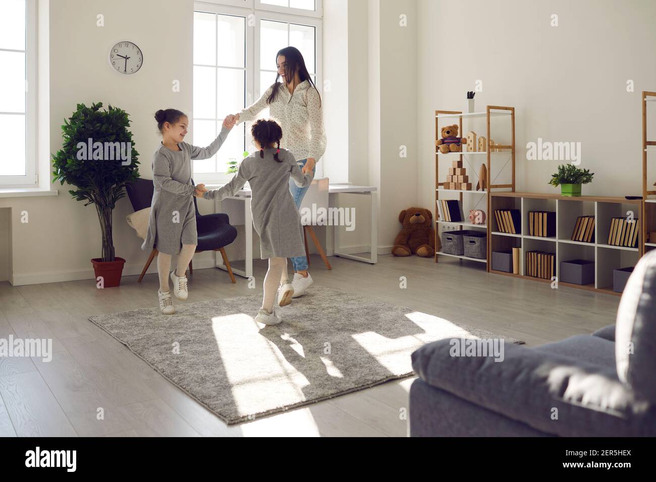 Fröhliche Mutter mit Zwillingstöchtern, die zu Hause Spaß haben und die Hände tanzen. Stockfoto