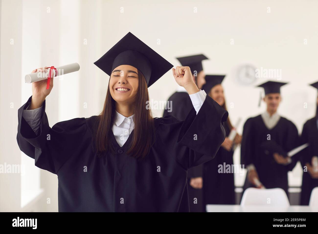 Porträt einer jungen Studentin, die mit geschlossenen Augen glücklich ist und ein Diplom hält. Stockfoto