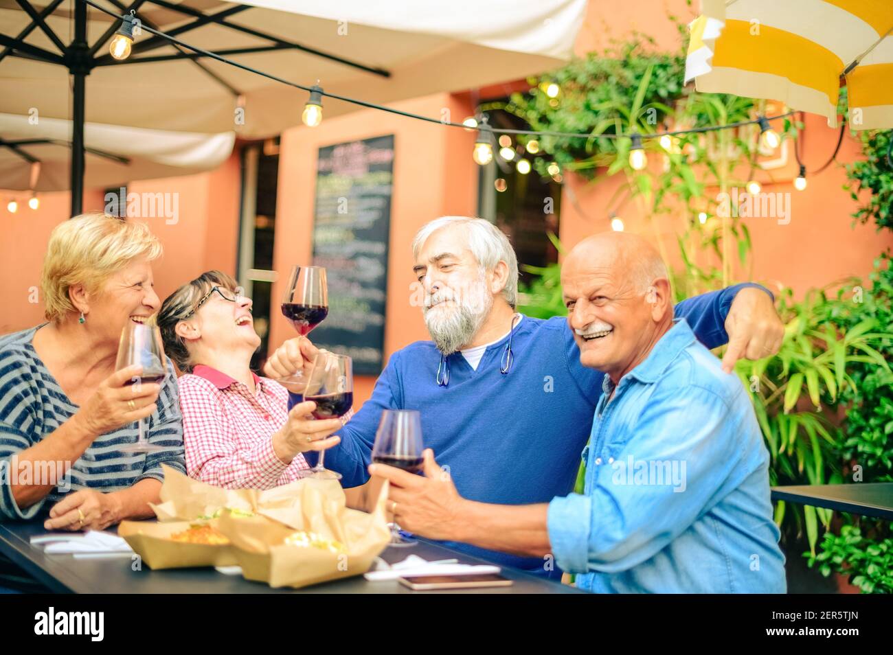 Ältere Leute lachen und rösten Rotwein im Restaurant - Freundschaftskonzept mit glücklichen reifen Freunden, die Spaß zusammen haben Zuhause im Garten Stockfoto
