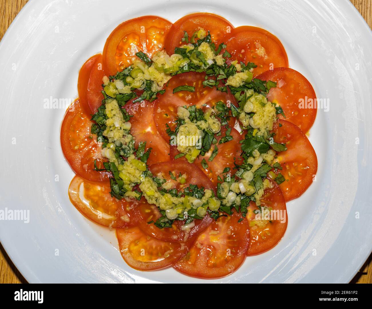 Nahaufnahme von dünn geschnittenem Tomatencarpaccio mit Kräutern, Frühlingszwiebeln und Ingwerdressing auf einem weißen Teller Stockfoto