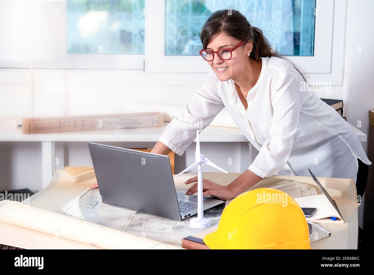 Lächelnd hübsche Frau Zeichnung Blaupause auf dem Tisch arbeiten an Notebook Stockfoto