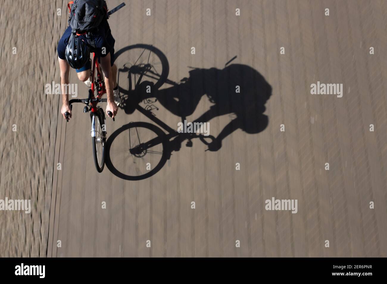 Schwenk von oben von einem jungen Mann reiten seine Rennrad mit Sahrp Schatten auf dem verschwommenen Bürgersteig Stockfoto