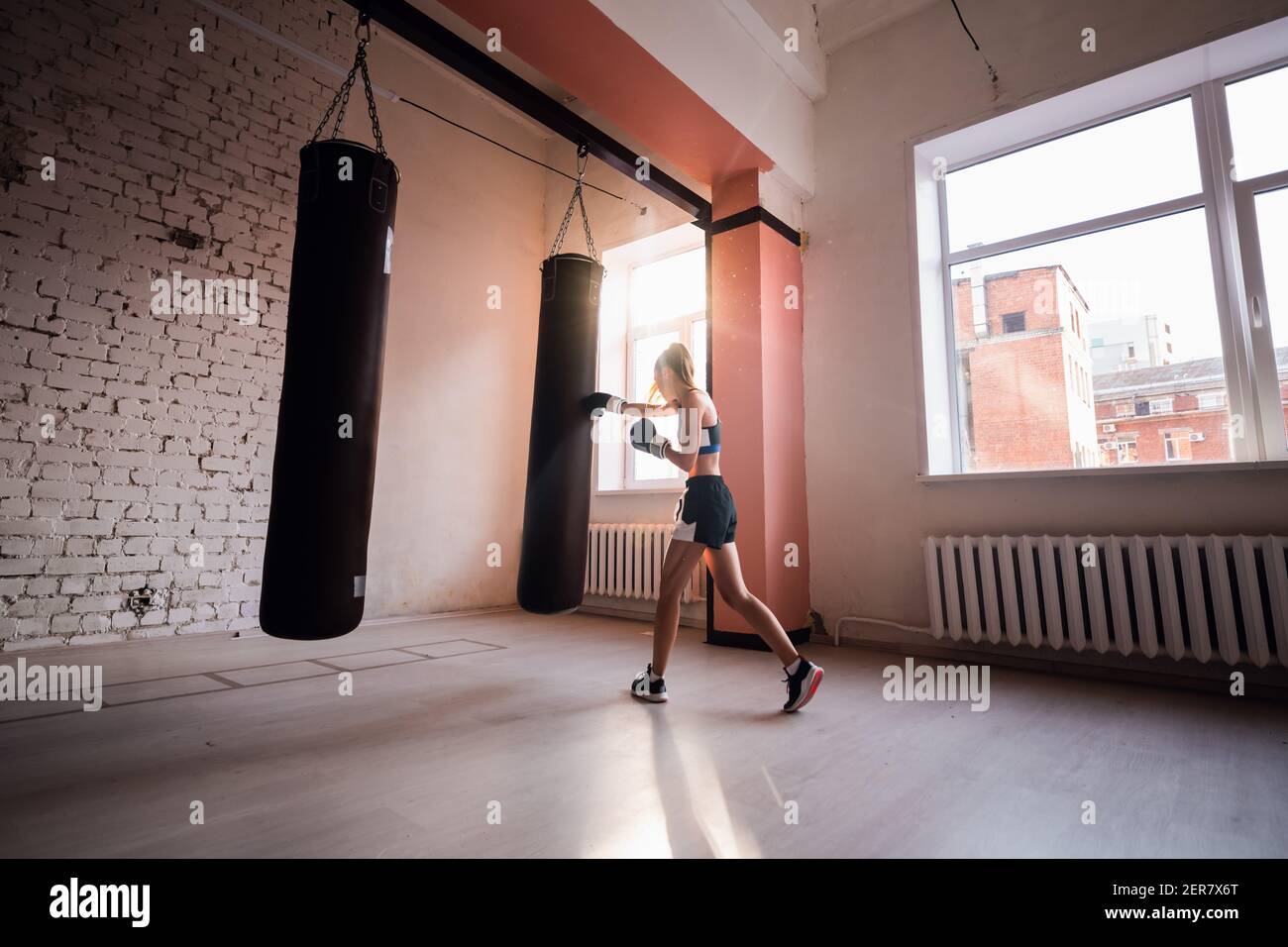 Weibliche Kickboxer schlagen Boxsack, während Staubpartikel fliegen in Sonnenfleck Licht Hintergrund. Stockfoto