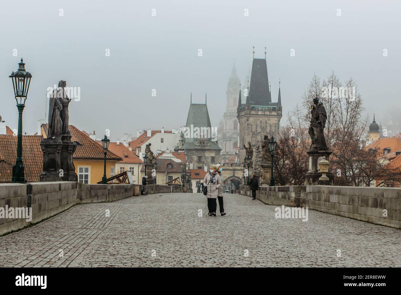Prag, Tschechische Republik - 24. Februar 2021.Frauen mit Gesichtsmaske gegen covid19 Coronavirus zu Fuß auf nebligen Karlsbrücke.Erwachsene mit OP-Maske Stockfoto