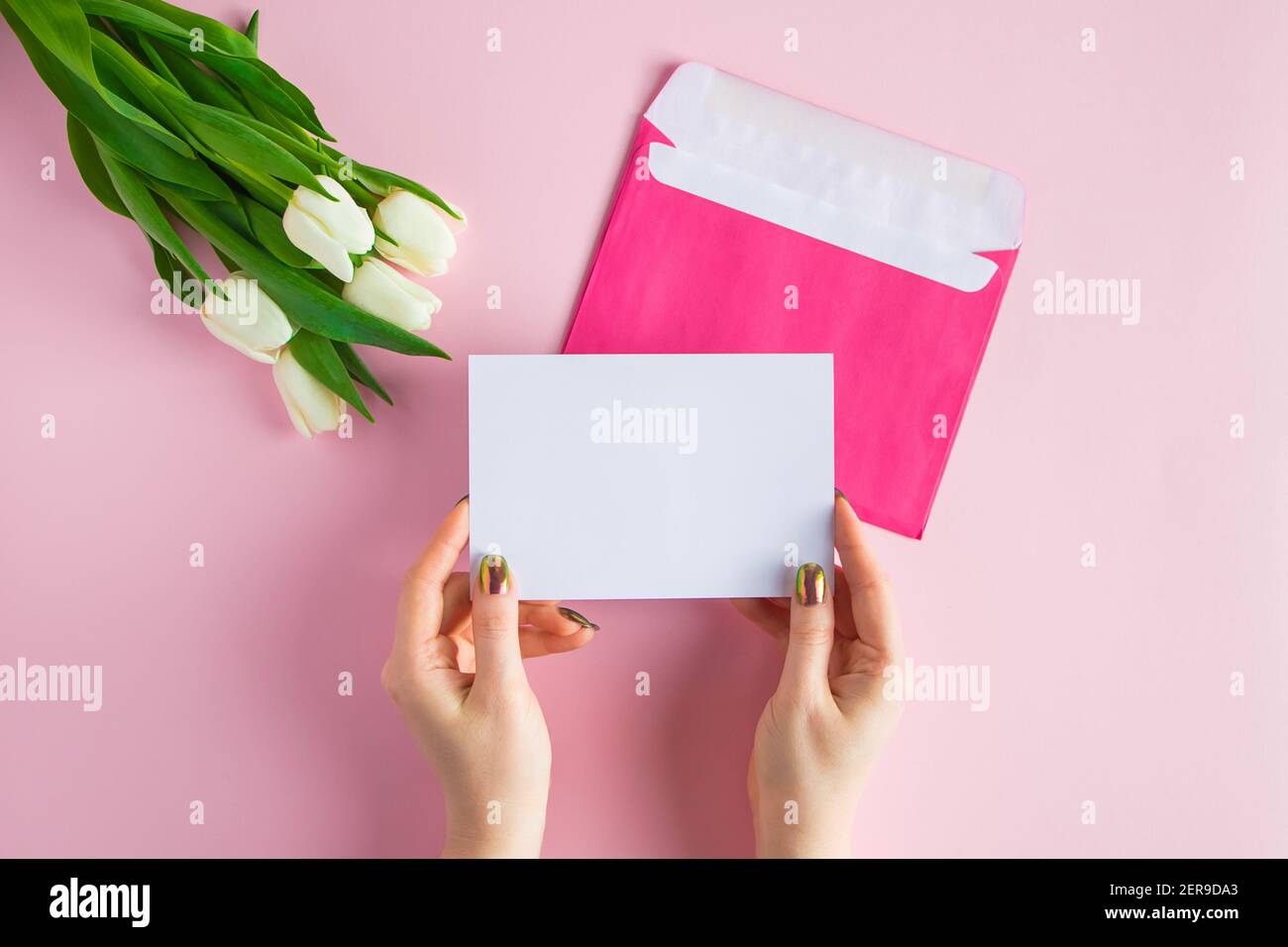 Frau hält Grußkarte in ihren Händen. Geschenk für Frühlingsferien. Bouquet von frischen Tulpen auf rosa Hintergrund. Stockfoto