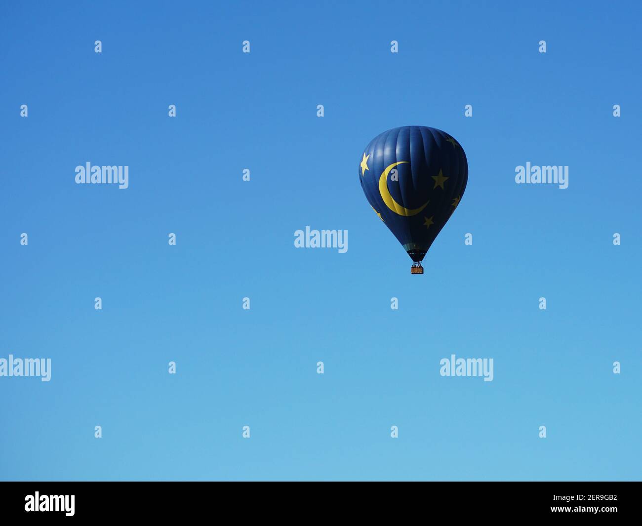 Blauer und gelber Heißluftballon vor dem Hintergrund des blauen Himmels und der Hügel. Aus der Ferne betrachtet. Stockfoto