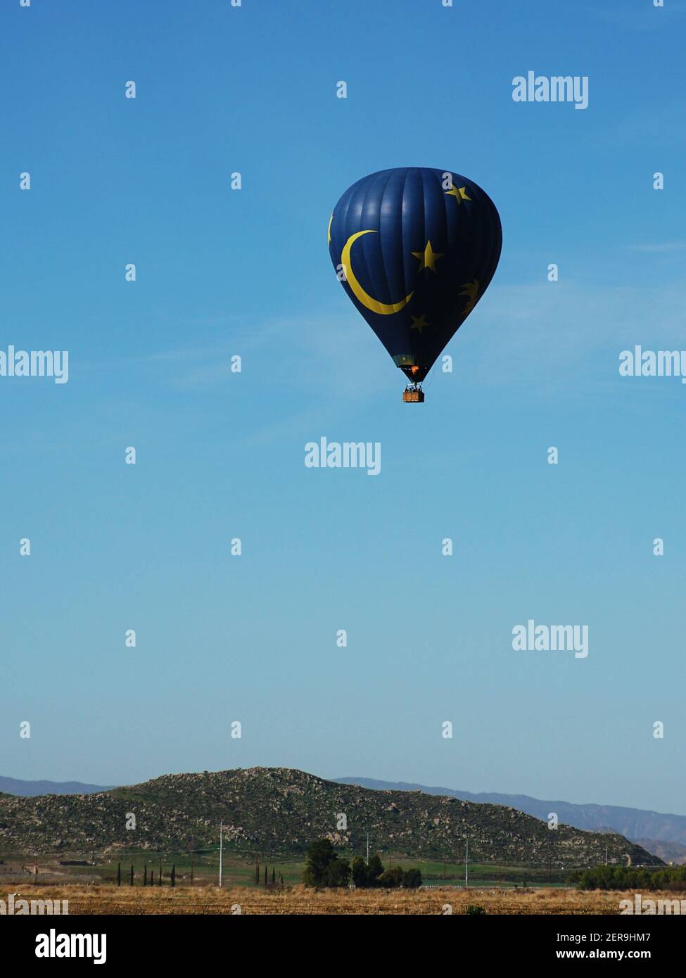 Blauer und gelber Heißluftballon vor dem Hintergrund des blauen Himmels und der Hügel. Von der Seite betrachtet. Stockfoto