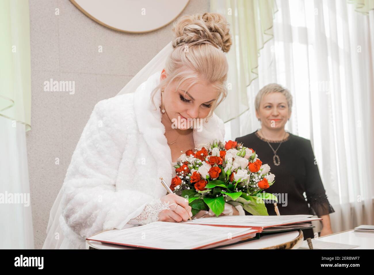 Attraktive niedliche Braut der europäischen blonden Auftritt setzt eine Signatur über die Zustimmung Ehe auf der Hochzeit. Weißrussland, Region Minsk - 23. Januar 202 Stockfoto