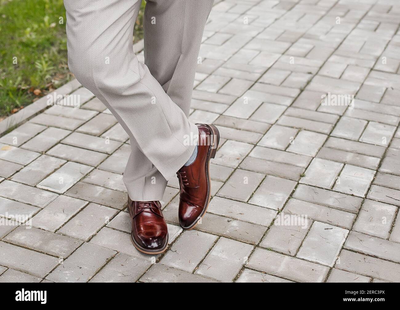Die Beine des Mannes sind Bein für Fuß in hellen Hosen und braune Schuhe stehen auf Pflasterfliese. Stockfoto