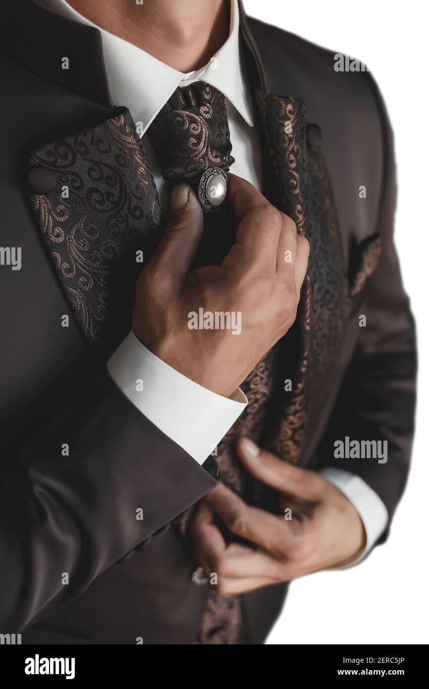 Ein Mann in einem weißen Hemd und einem braunen Luxus-Anzug passt die Krawatte mit der Perle mit den Händen aus nächster Nähe an. Stockfoto