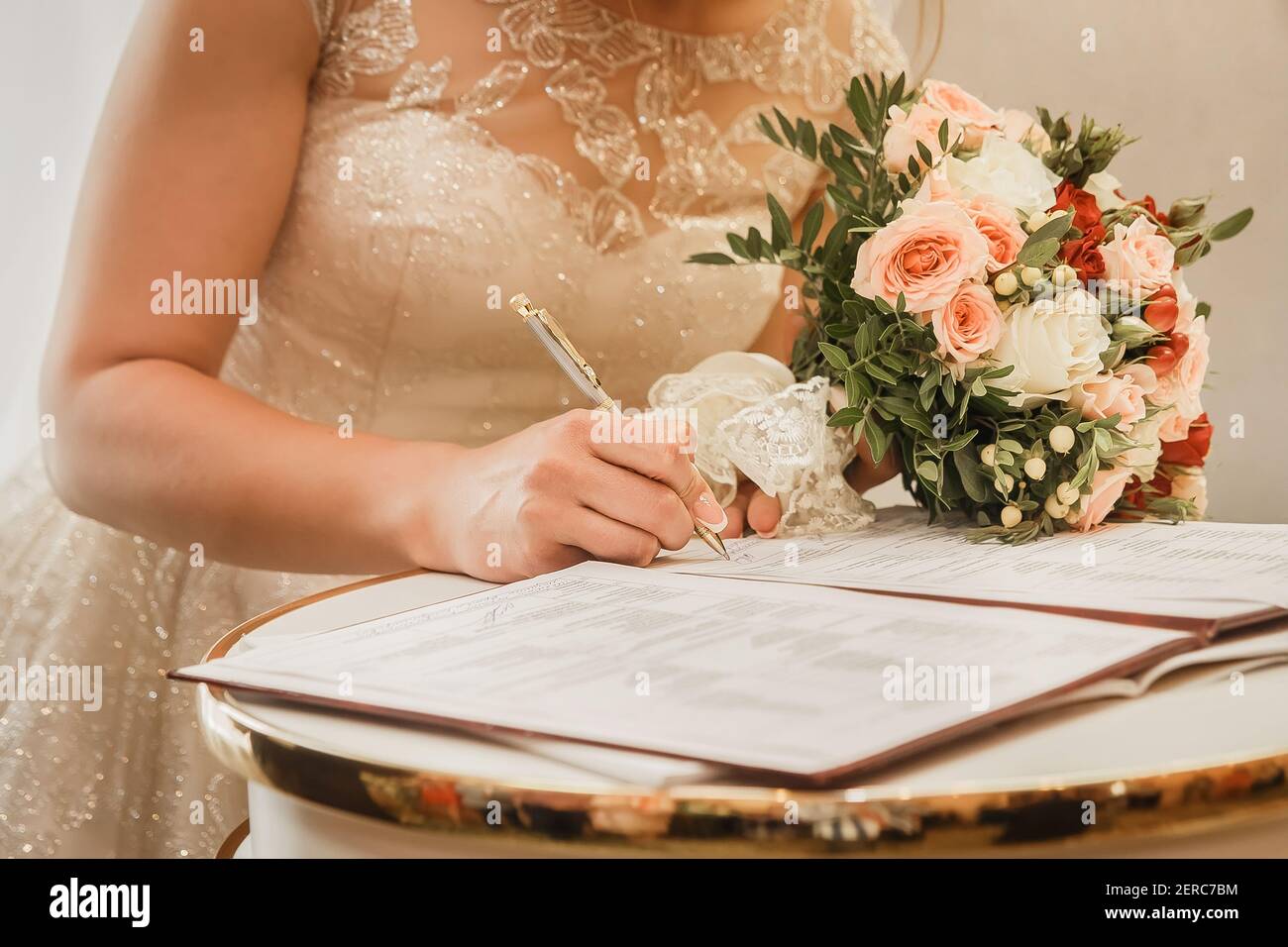 Die Hand der Braut setzt den Signaturstift auf die Zustimmung, bei der Hochzeit Nahaufnahme zu heiraten. Stockfoto