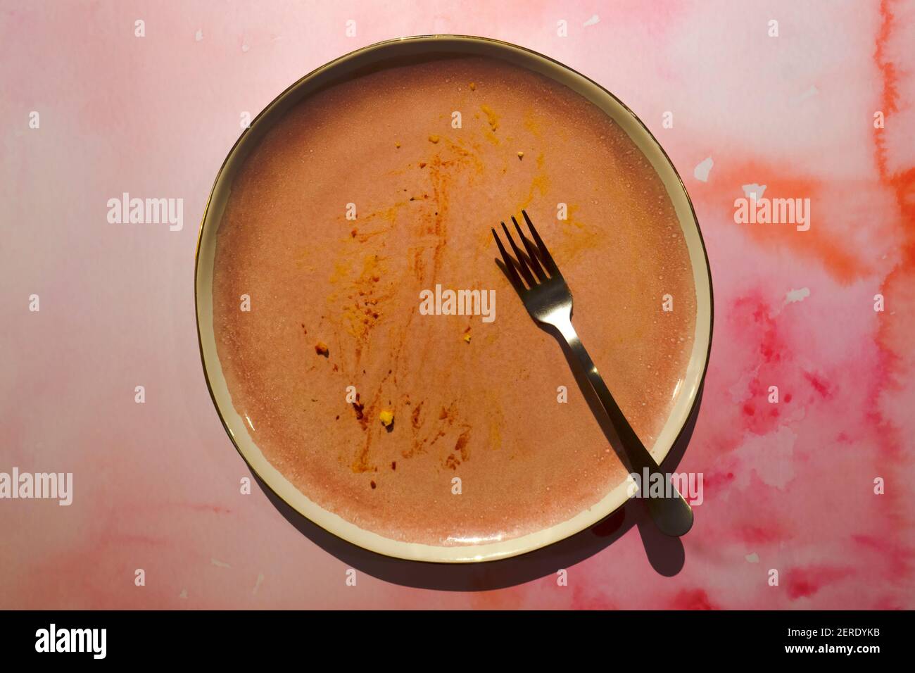 Schmutzige rosa Keramikplatte mit Speiseresten auf einem rosa grunge Hintergrund. Flache Platte mit Gabel leeren. Hintergrund des Tisches nach dem Ende des Mittagessens Stockfoto