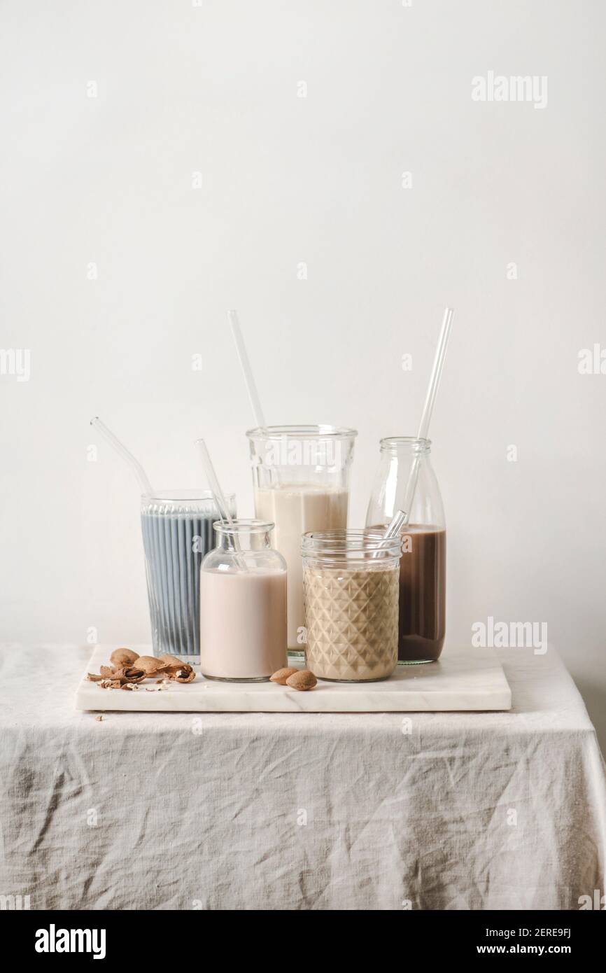 Milchfreies Milchsortiment mit verschiedenen Geschmacksrichtungen. Mandelmilch mit blauen Matcha, Beeren, Kaffee, Zimt, Kakao in Flaschen und Gläser auf der Theke, Stockfoto