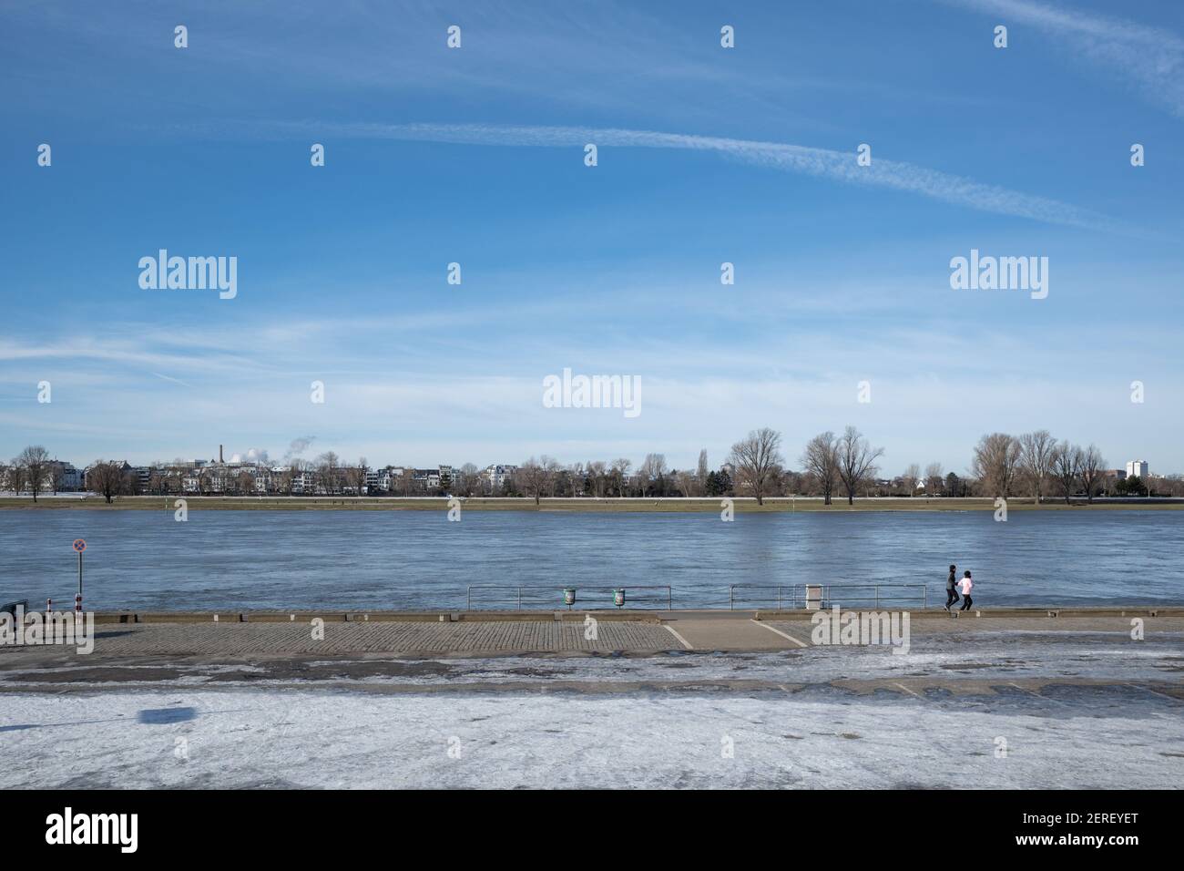 Outdoor sonniger Landschaftsblick, zwei Läufer laufen auf der Uferpromenade am Rhein am Rheinpark Golzheim in Düsseldorf, Deutschland im Winter. Stockfoto