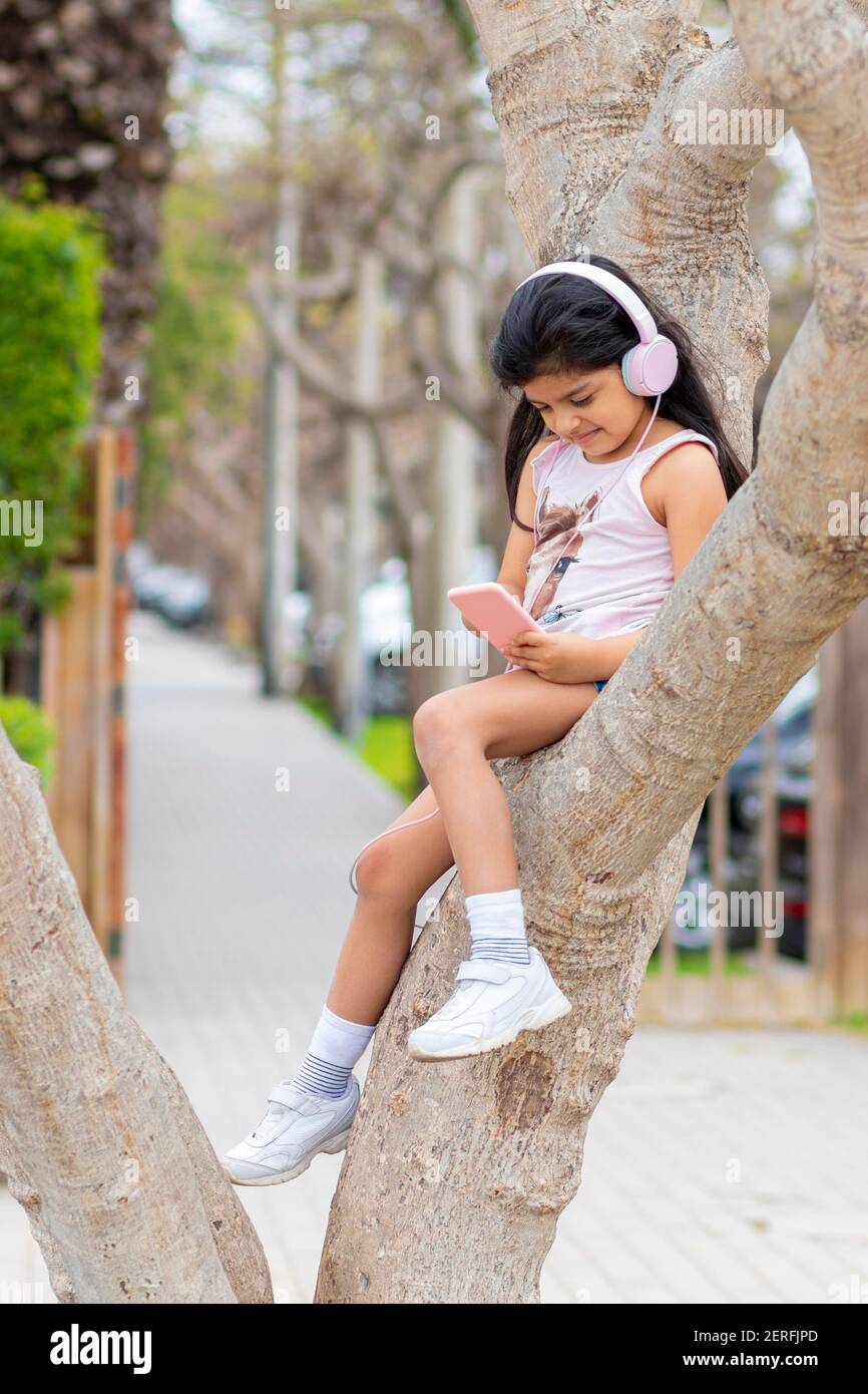 Das kleine Mädchen hört Musik mit ihren Kopfhörern an Ein Baum Stockfoto