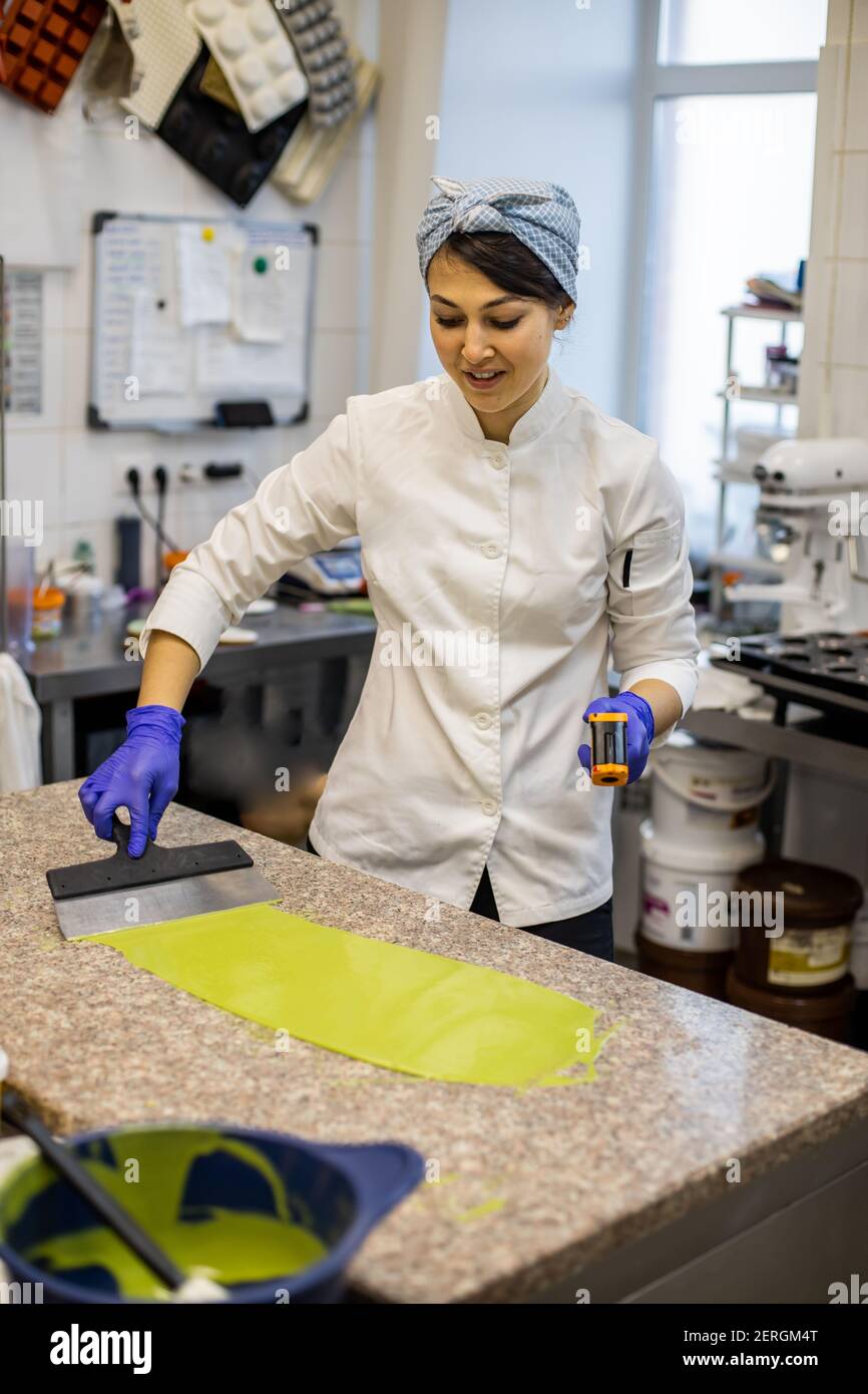 Frau Konditor in Uniform Gießen flüssige Matcha Tee Schokolade auf Tisch aus Schüssel bei der Küche Stockfoto